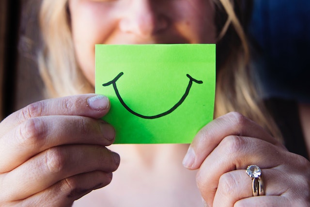 person holding a green post-it note with a smile drawn on it in front of their face